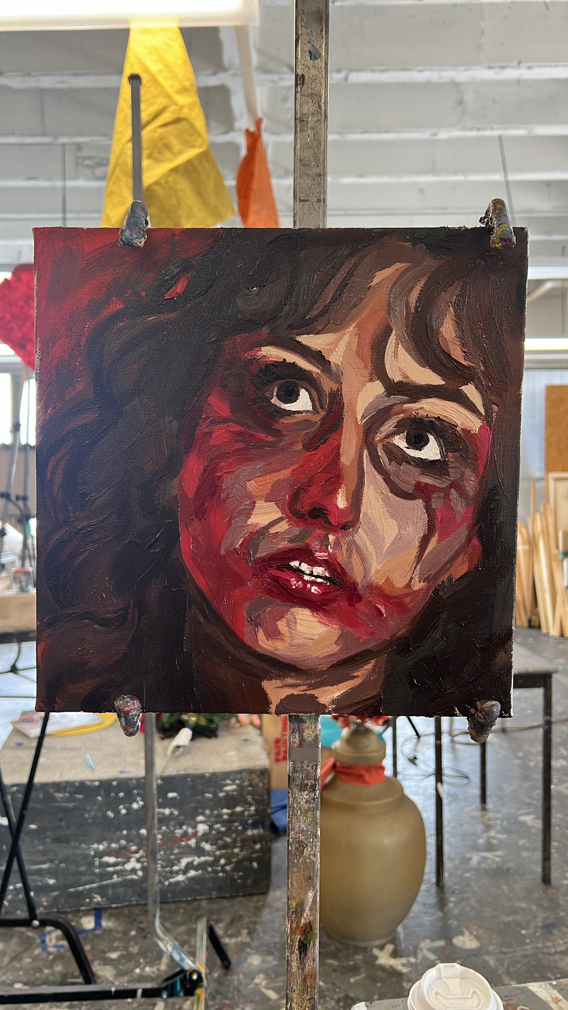 An expressive oil portrait in deep reds and browns of a woman looking upward, photographed on an easel in a studio